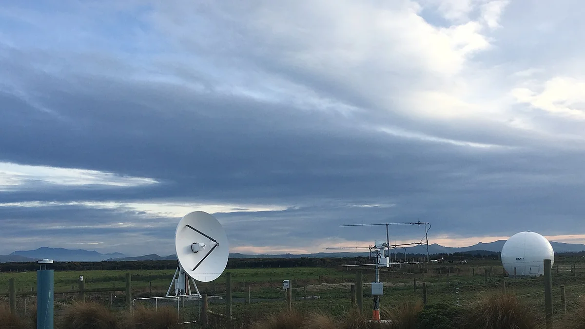 Satellite dish and antennas at a ground station under heavy clouds