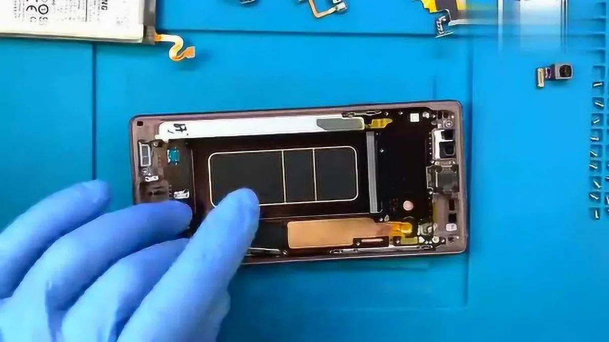 Gloved hands pointing inside a disassembled smartphone on a repair mat